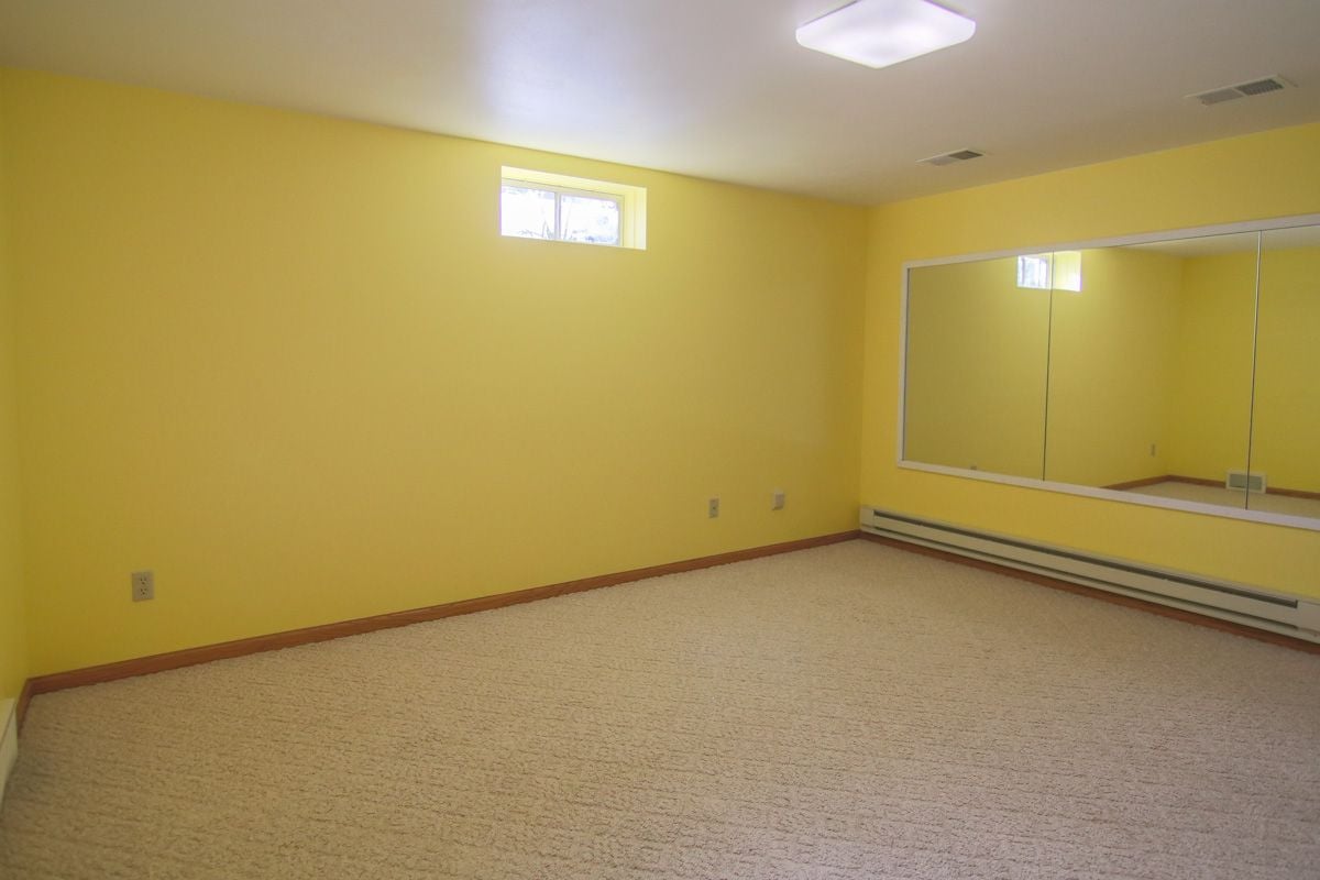 Empty carpeted room with yellow walls and a wide wall mirror.
