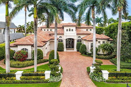 Mediterranean-style home with an arched entry and palm-lined brick driveway.
