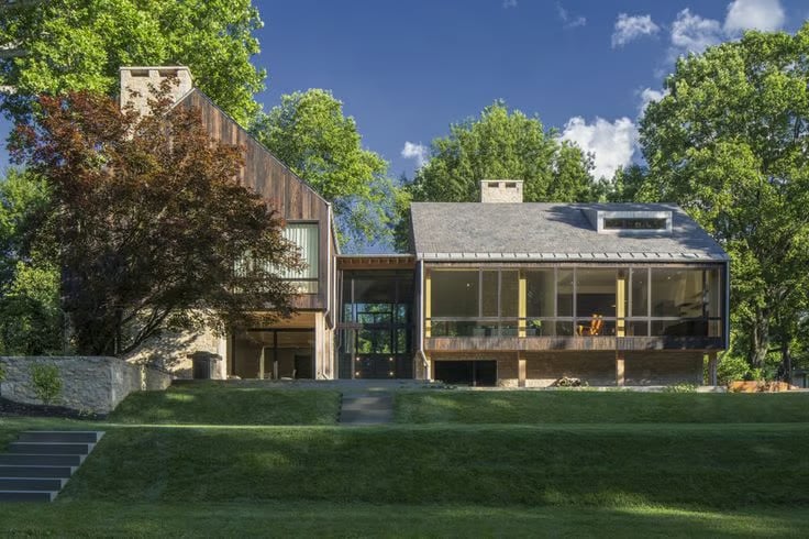 Modern home with expansive glass windows, wood siding, and a sloped lawn.