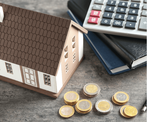 Miniature house model beside a calculator, books, and coins.