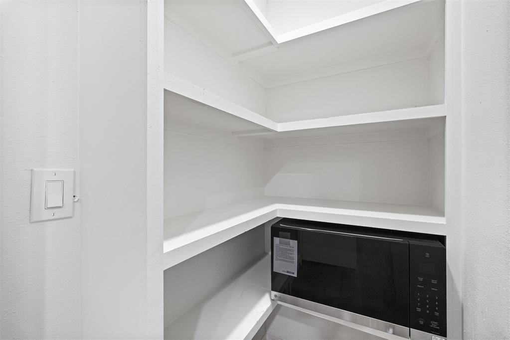 Empty pantry with white corner shelves and a black microwave.