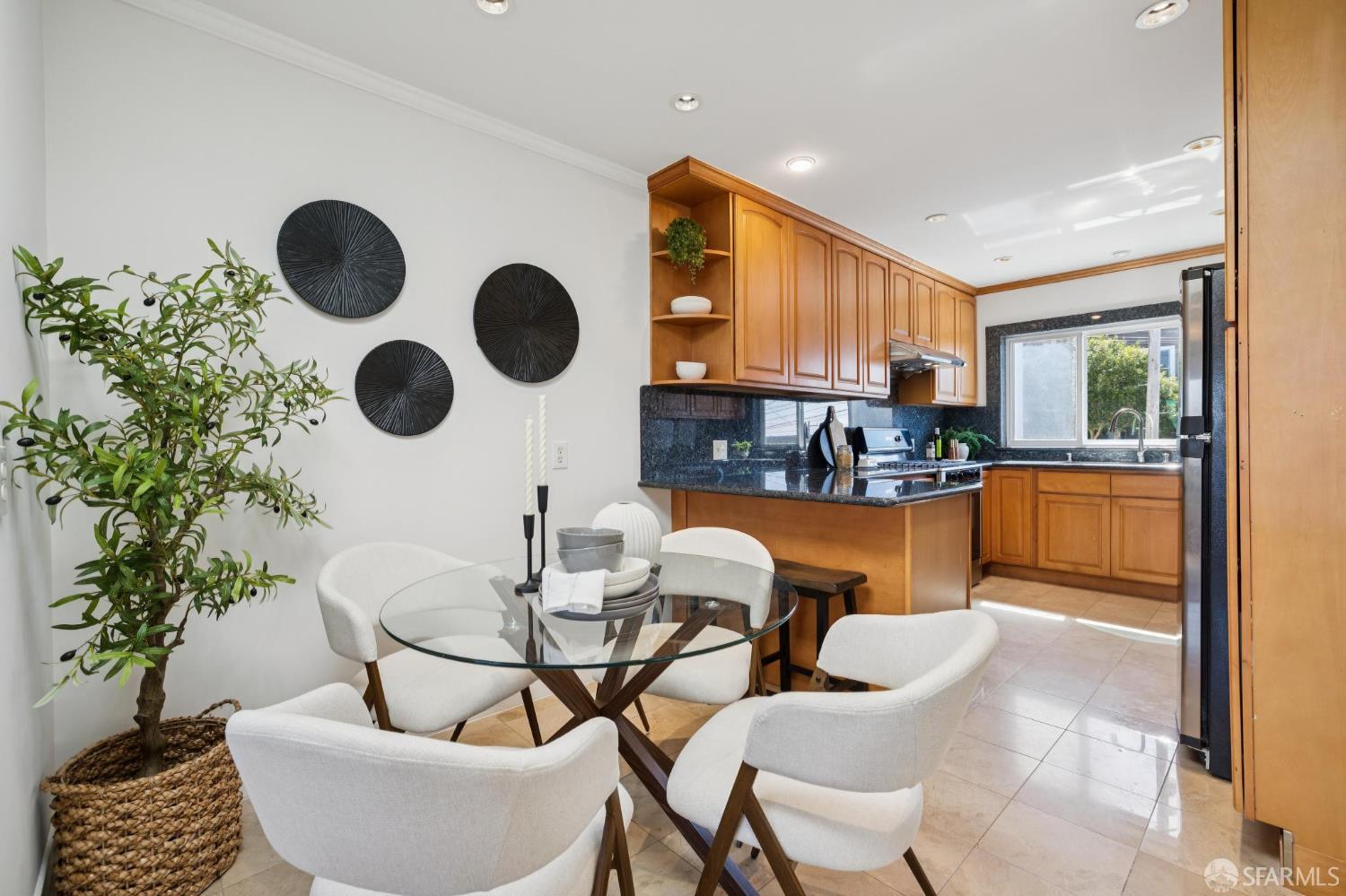 Kitchen and dining area with warm wood cabinets, dark counters, and a glass table with white chairs.