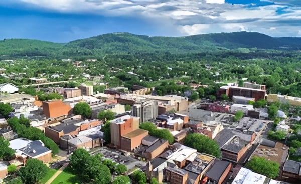 Aerial view of a neighborhood with low-rise buildings, leafy streets, and green hills in the distance.