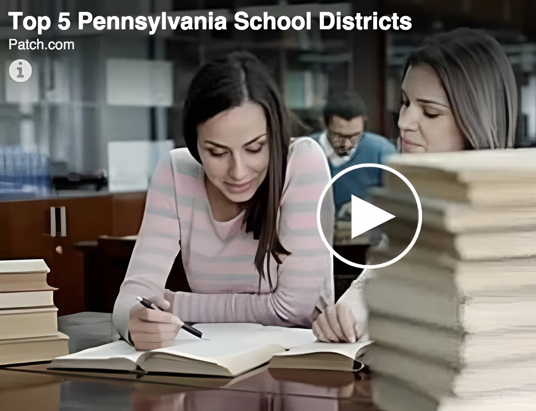 Woman writes in an open book at a desk, with other people studying behind her.
