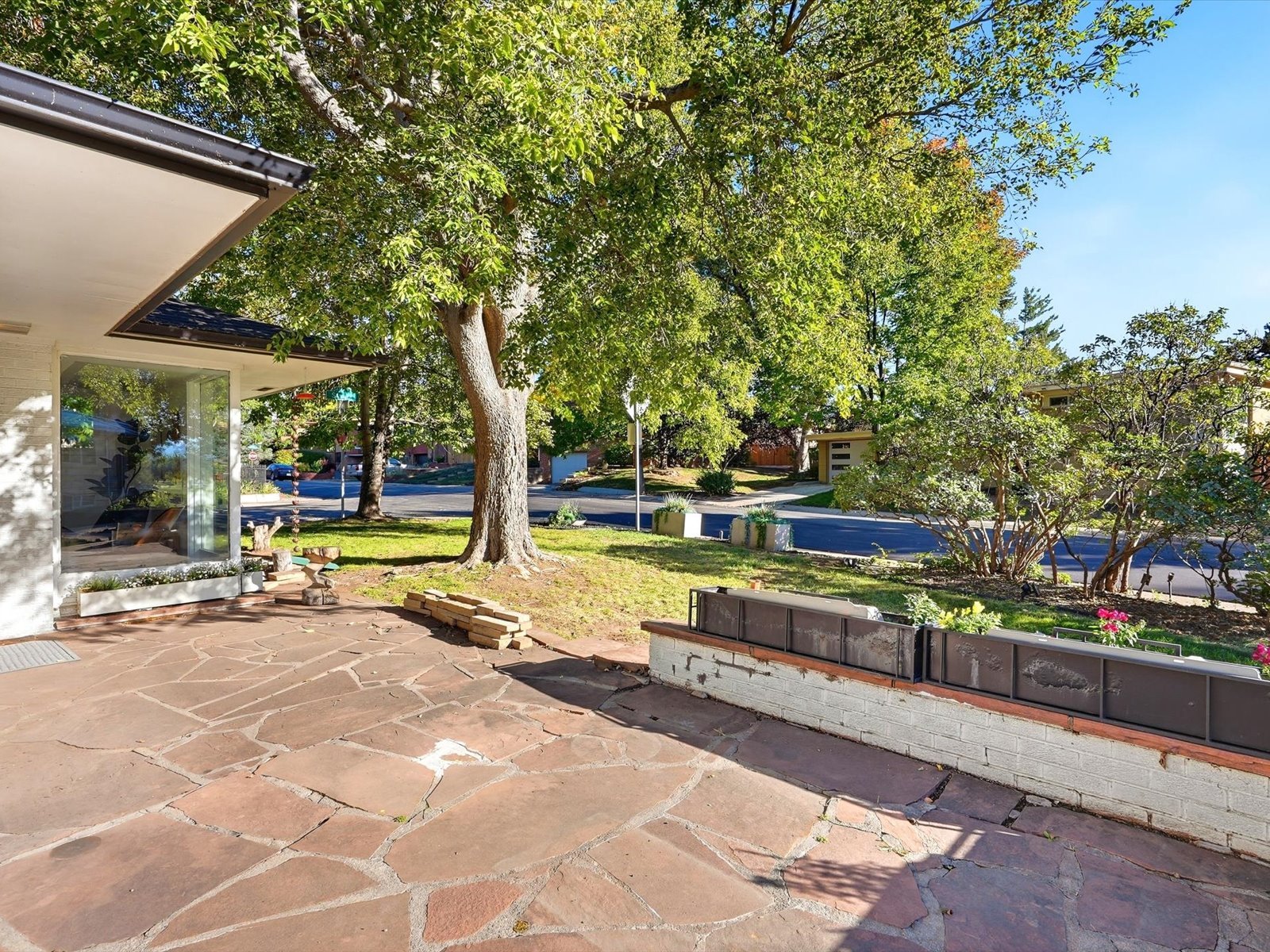 Modern home’s flagstone patio and front yard beneath a large shade tree.