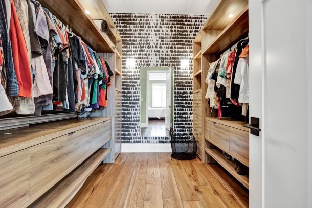 Walk-in closet with wood cabinetry, clothing rails, and a doorway at the far end.