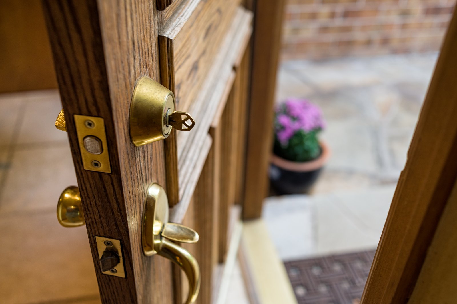 Open wooden front door with key in brass lock, stone path and potted flowers beyond.