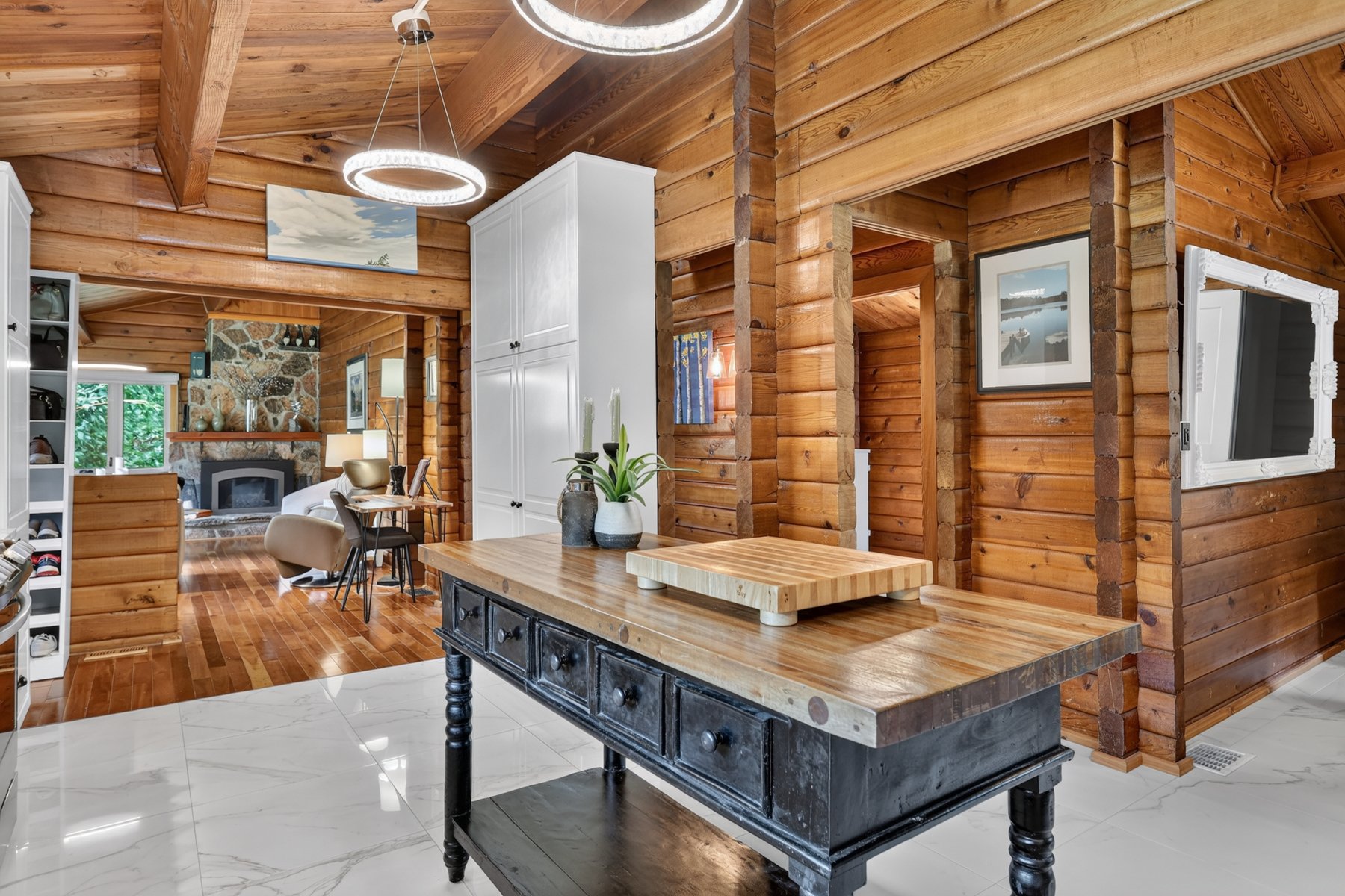 Log cabin kitchen with a rustic island, timber walls, and a stone fireplace in the adjoining living area.