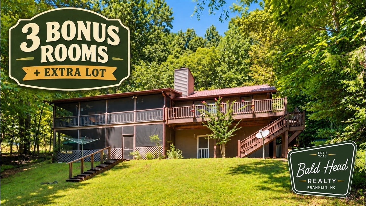 Wooded home with an elevated deck, exterior stairs, and a sunlit lawn.