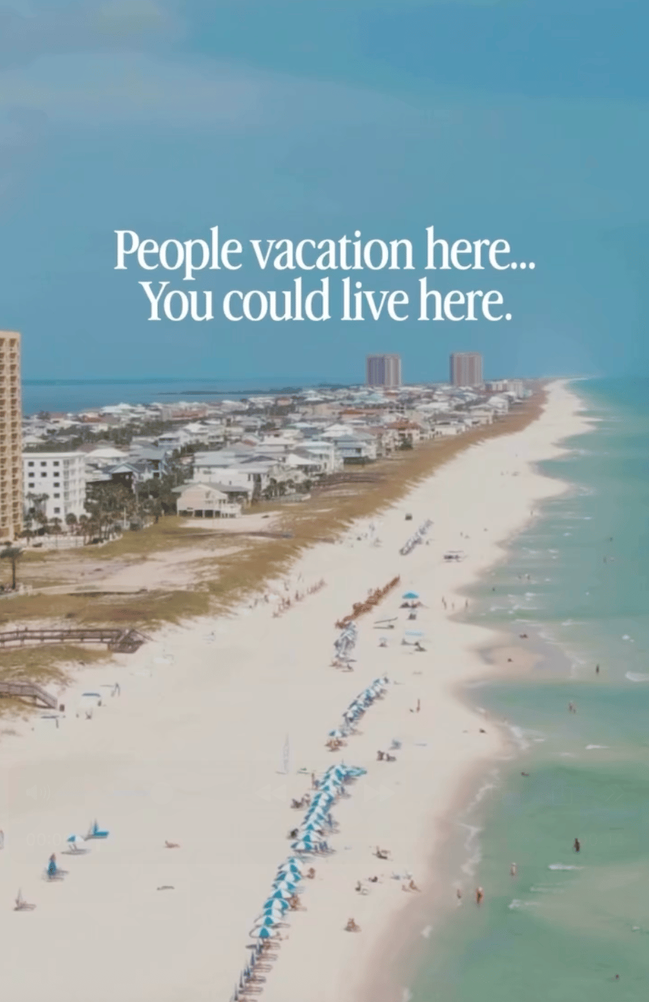 Aerial coastal beach with rows of umbrellas, turquoise water, and beachfront buildings.