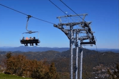 Chairlift above autumn-colored mountain ridges under a clear blue sky.