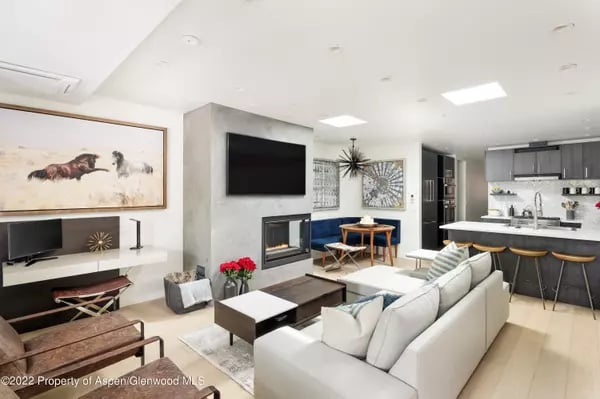 Open-plan living room with a white sectional, fireplace, and kitchen island with bar stools.