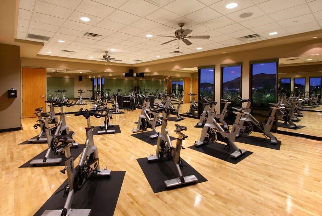 Fitness room with rows of stationary bikes, mirrored walls, and windows overlooking hills.
