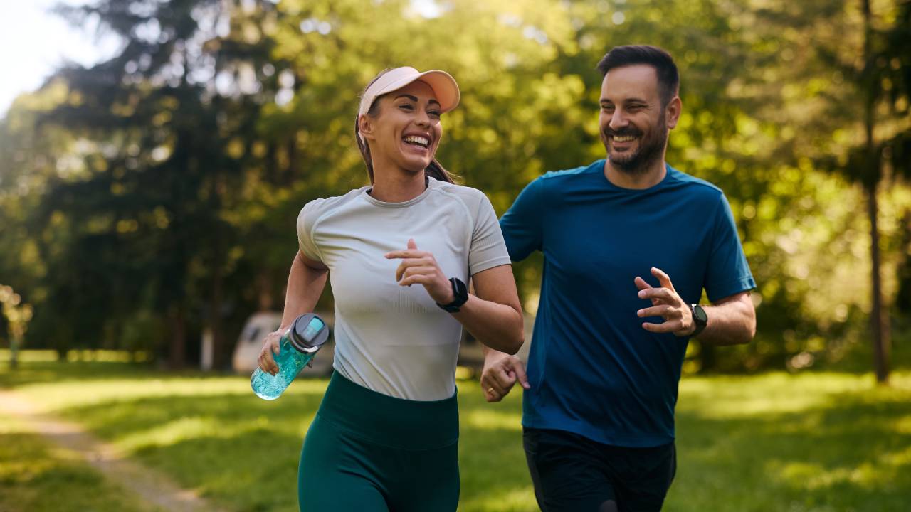 Couple jogging through a sunny park, embracing the healthy lifestyle in Aspen with fresh air and scenic green surroundings.
