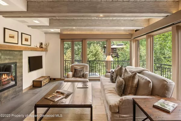 Living room with exposed beams, a stone fireplace, and a balcony overlooking trees.