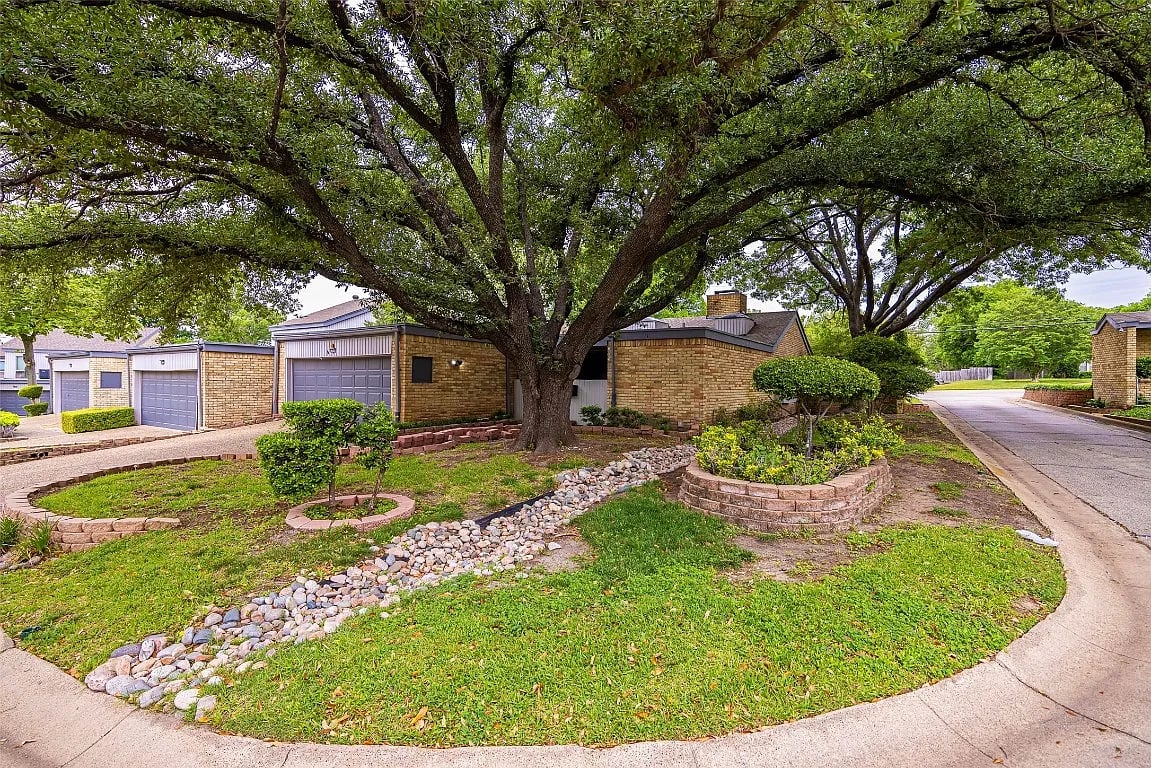 Brick home beneath a sprawling oak tree, with garage doors and a landscaped front yard.