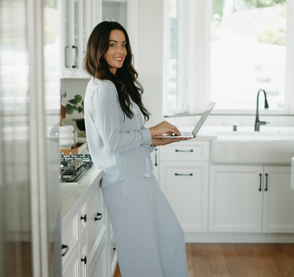 Kyndal DeJurnett standing in kitchen holding laptop posing for photo