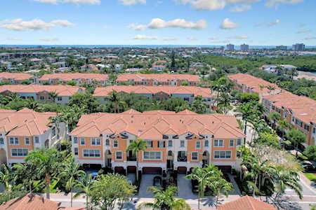 Aerial view of terracotta-roofed townhomes among palm trees, with a distant skyline.