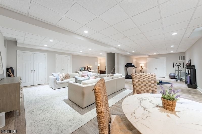 Furnished basement recreation room with white sofas, a marble-top table, and exercise equipment.