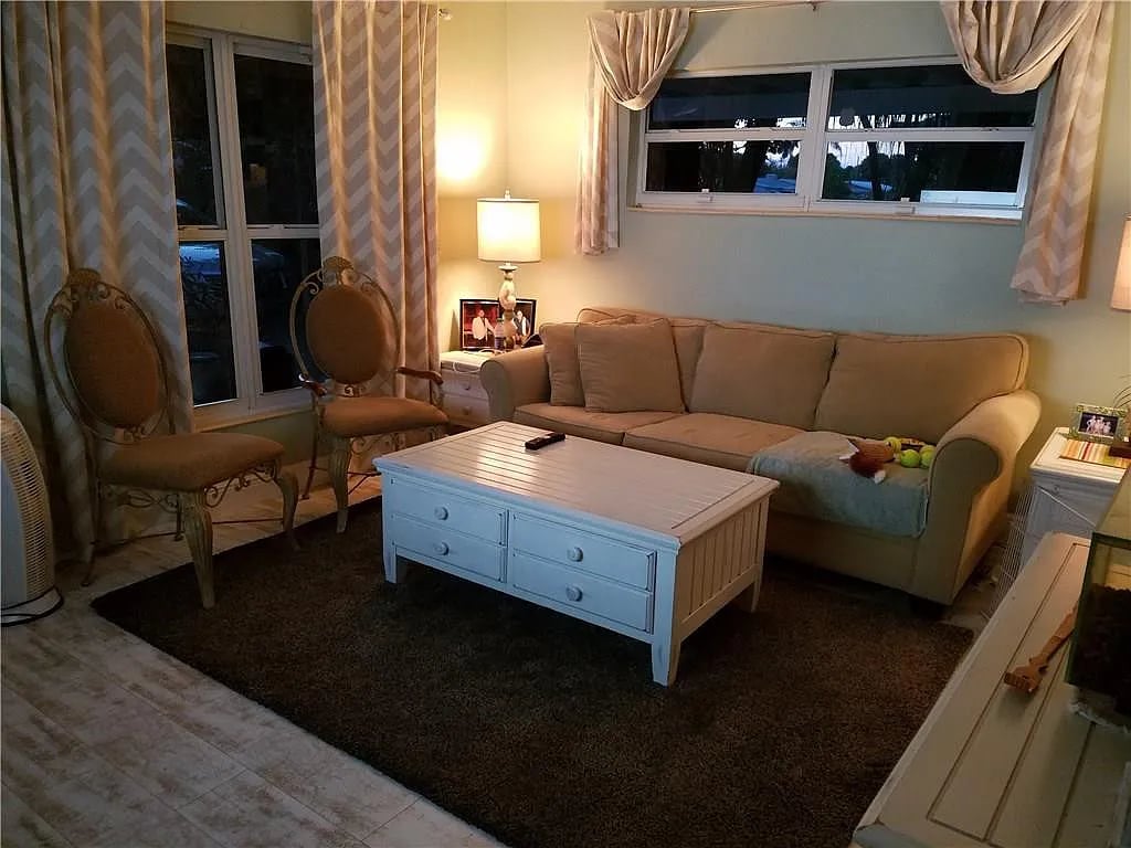 Living room with a tan sofa, two chairs, and a white coffee table on a dark rug.