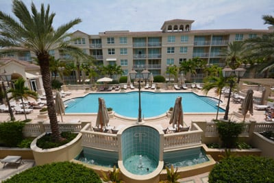 Condominium courtyard pool with palm trees, lounge seating, and the residential building behind it.