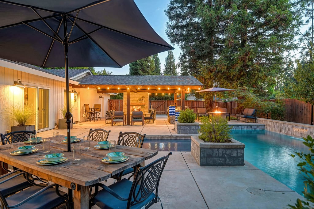 Backyard pool beside a covered patio with string lights and an umbrella-shaded dining table.