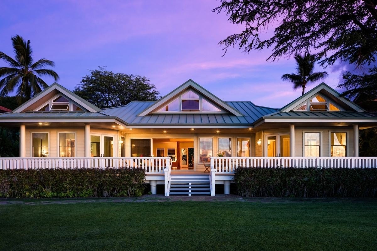 Single-story home with a broad white veranda and blue metal roof at dusk.