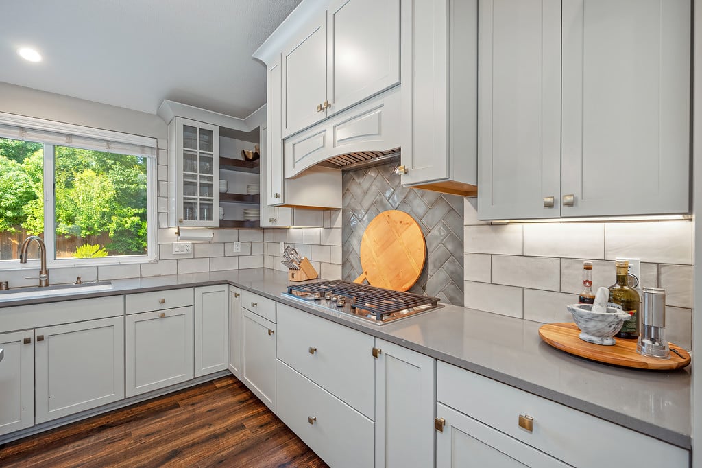 Kitchen with white cabinets, a gas cooktop, patterned backsplash, and a large window overlooking trees.