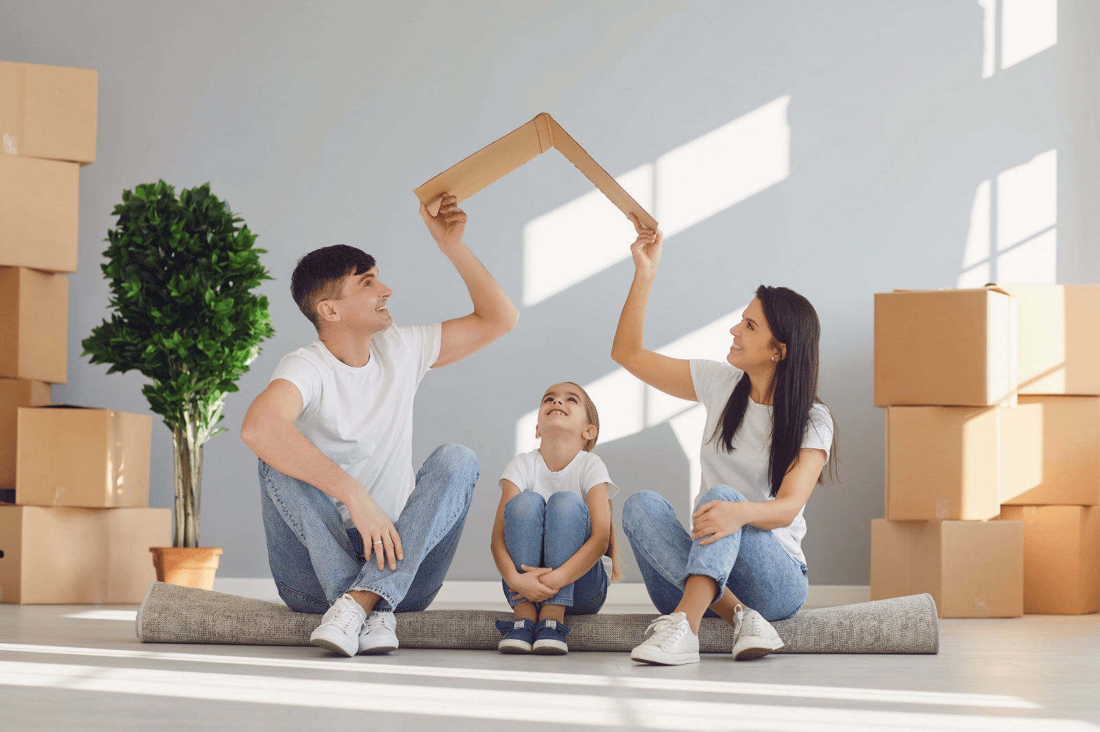 Family sits among moving boxes as parents hold a cardboard frame above their daughter.