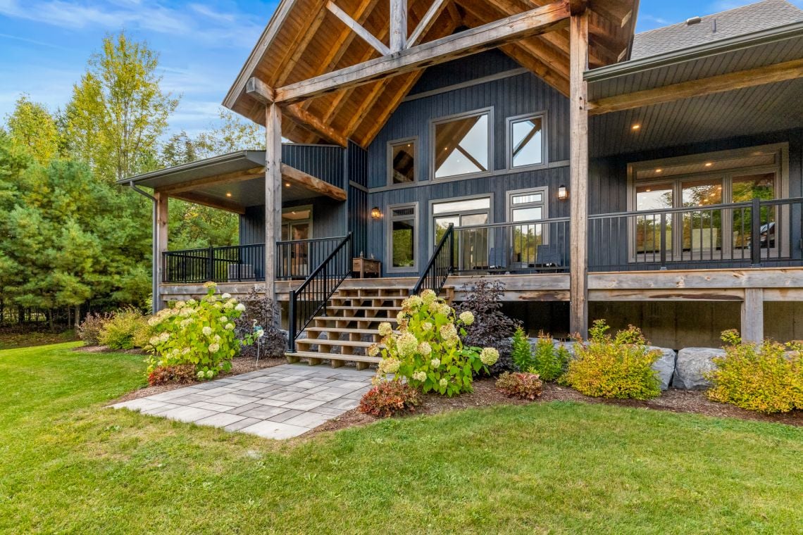 Dark blue house with a timber-framed porch, black railings, and landscaped front yard.