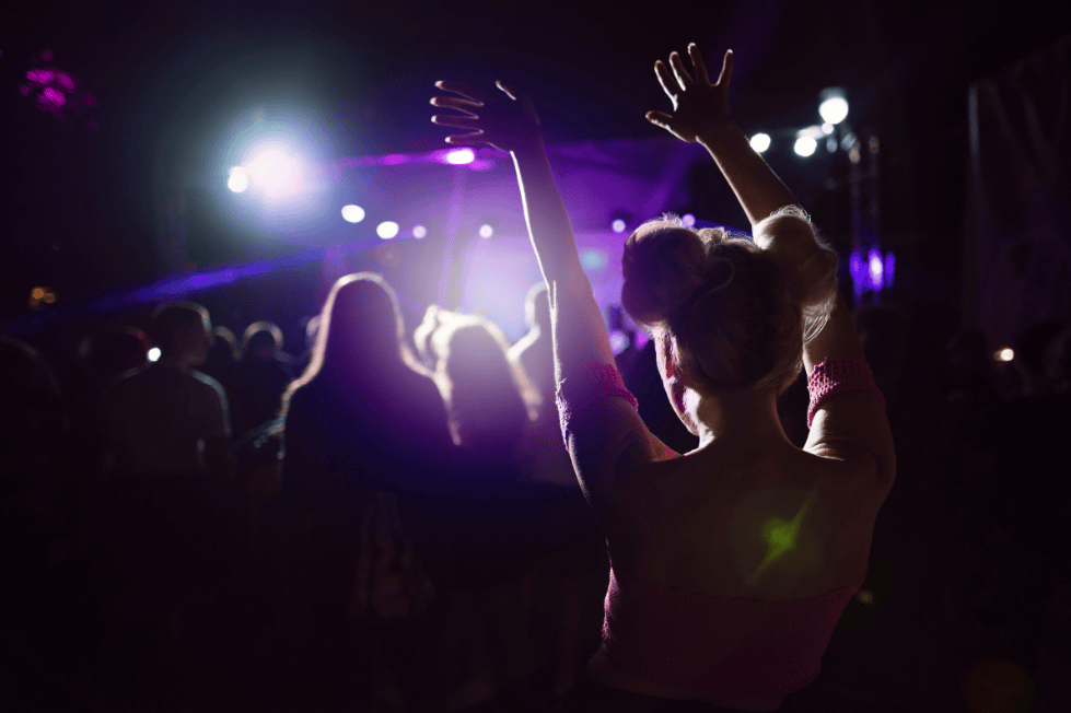 Person raising hands at concert crowd under bright stage lights