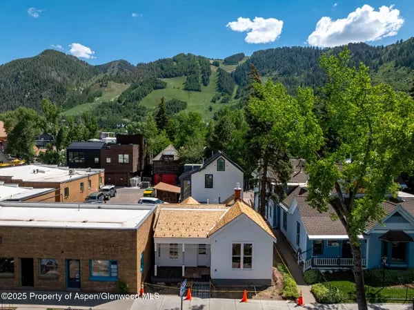 Aspen buildings below forested mountain slopes on a sunny day.