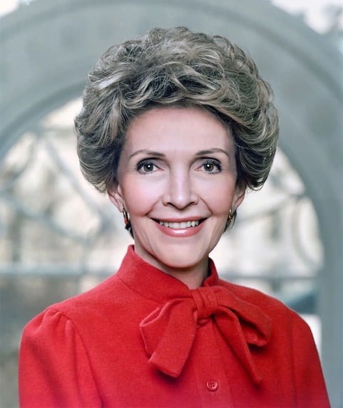 Nancy Reagan smiling in a red coat with a bow at the neck.