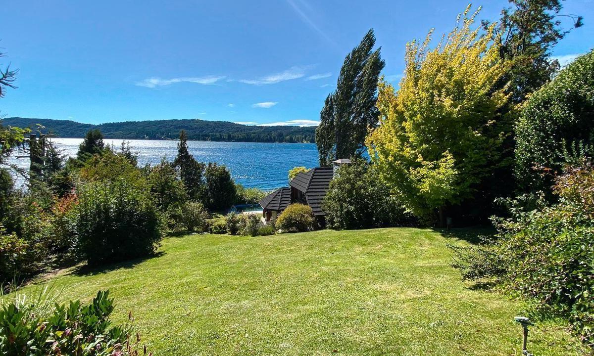 Lakefront property with a broad green lawn, trees, and distant wooded hills across the water.