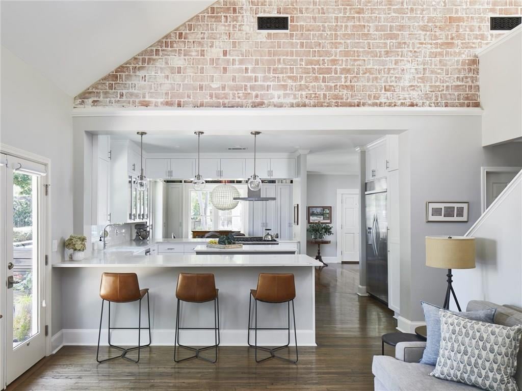Vaulted great room with a whitewashed brick accent wall and hardwood floors, open to the kitchen, in a Pemberton Heights home on Northwood Road in Austin, Texas. Architectural renovation by McWalters Collaborative.