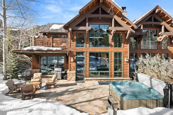 Mountain home with expansive windows, outdoor seating, and a hot tub on a snowy patio.