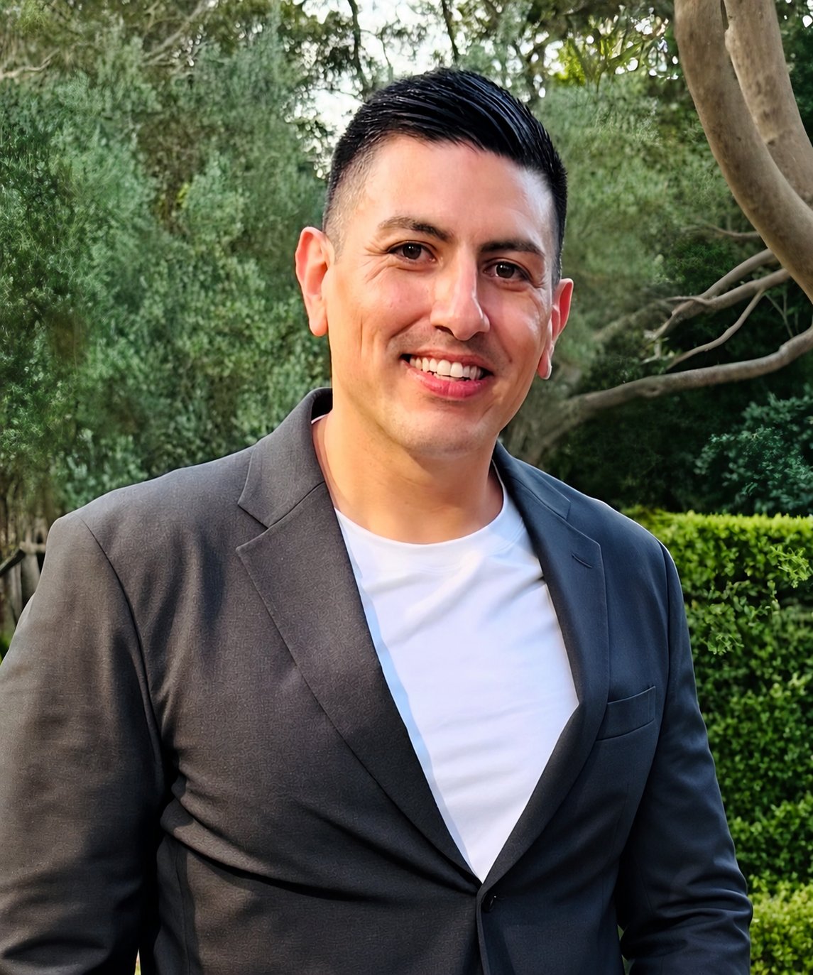 Johnathan Vigil smiling in a charcoal blazer and white shirt outdoors.