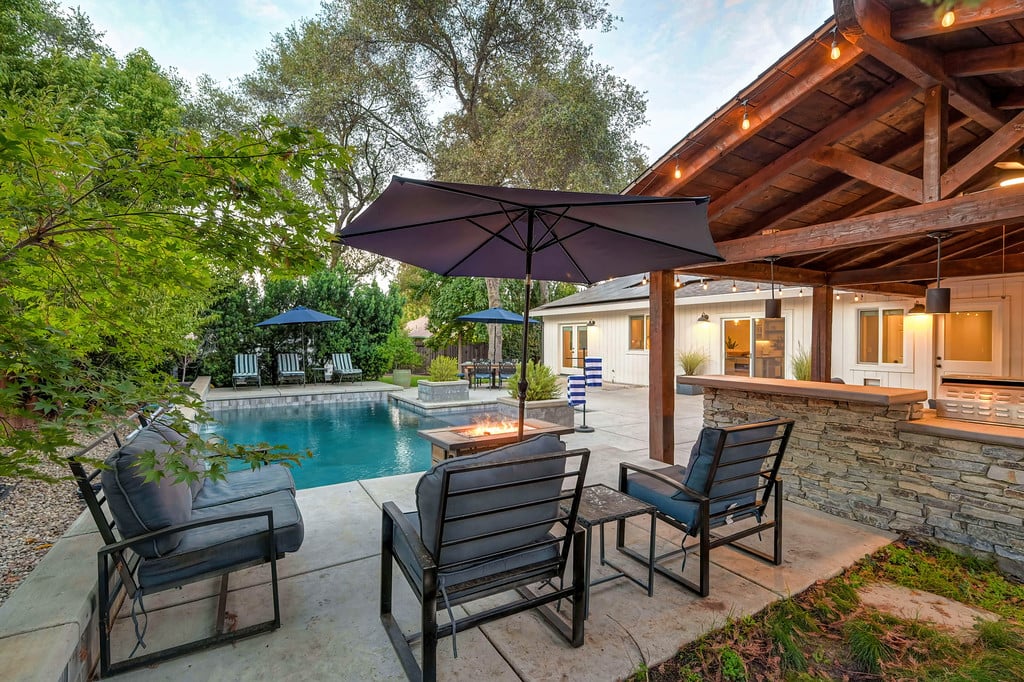 Backyard pool patio with covered stone bar, lounge seating, and a fire feature.
