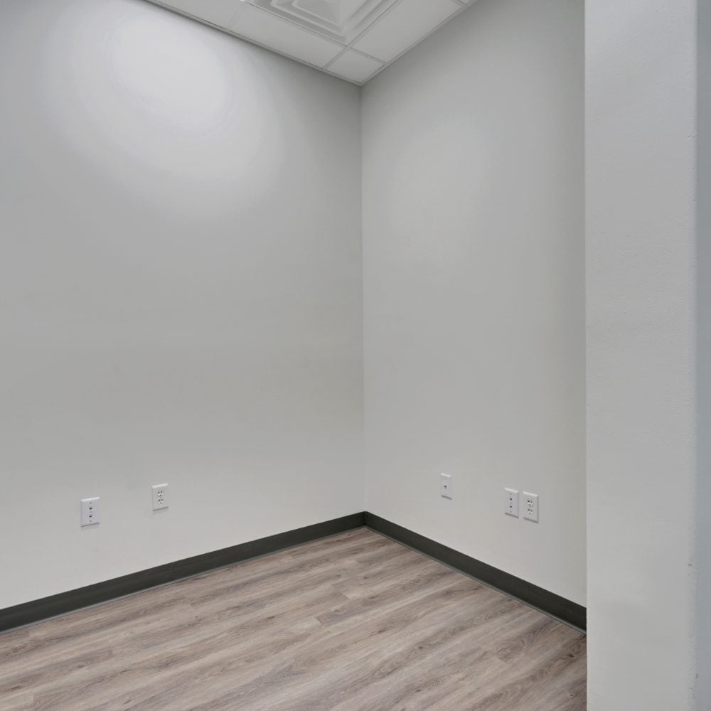 Empty room with gray wood-look flooring, wall outlets, and a suspended ceiling.