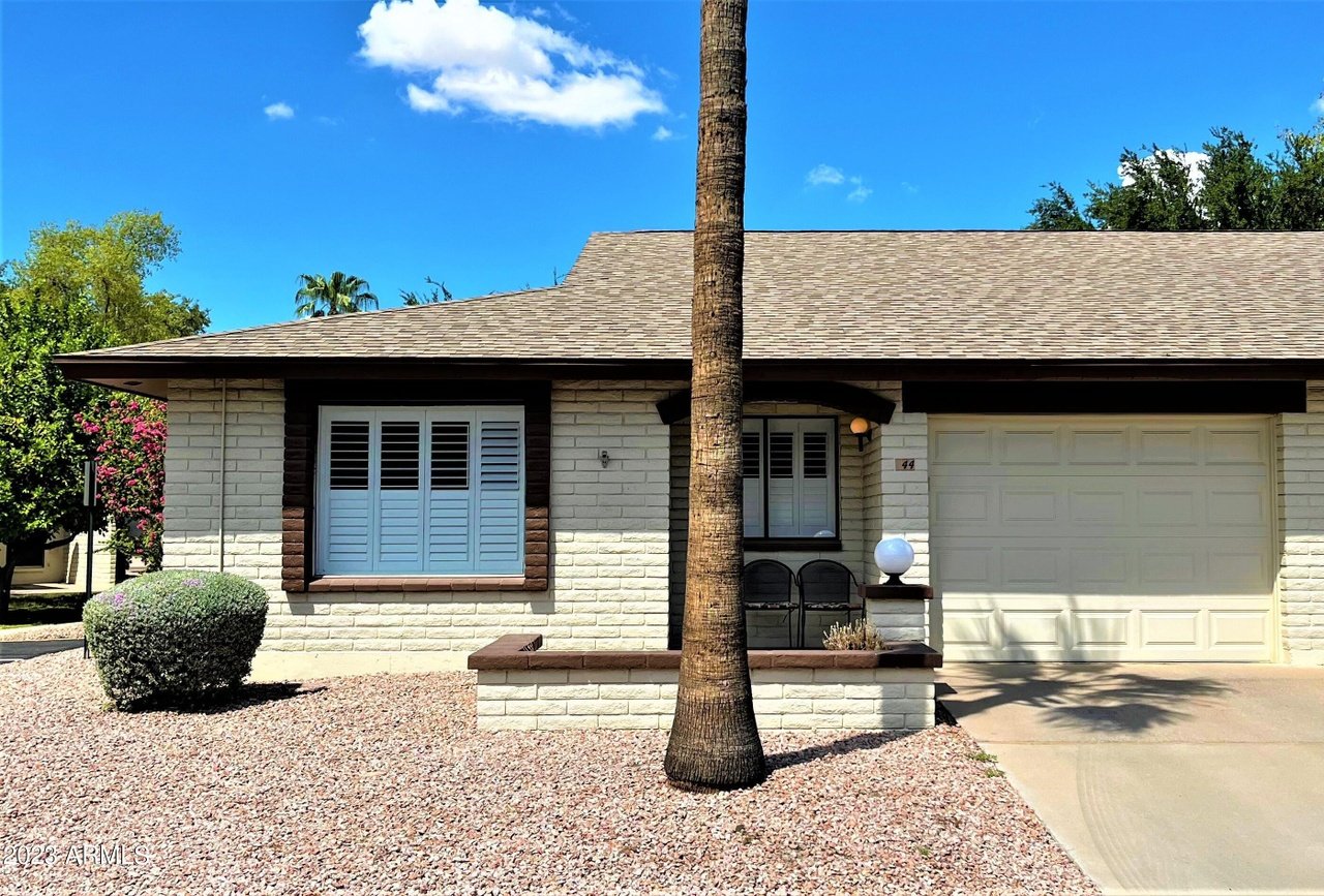 Single-story stone-front home with a two-car garage, palm tree, and gravel landscaping.