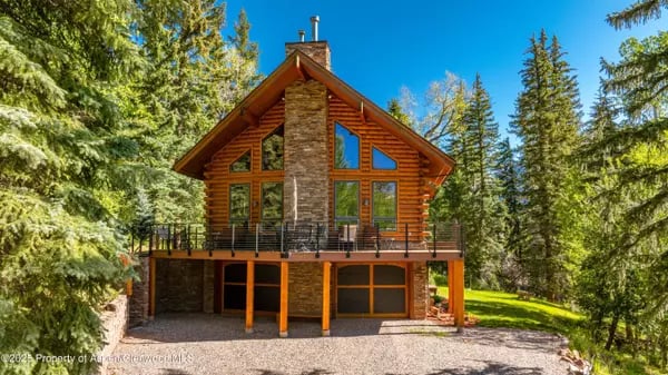 Timber and stone cabin with a broad deck, set among evergreen trees.