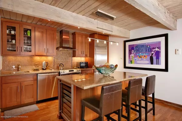 Kitchen with wood cabinetry, exposed ceiling beams, and a stone island with bar stools.