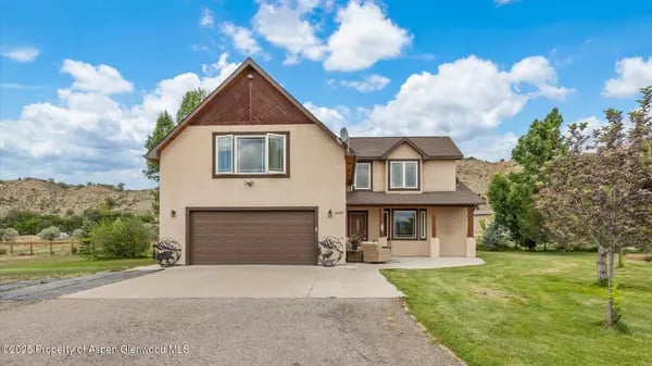 Two-story beige home with brown trim, a double garage, and a wide concrete driveway.