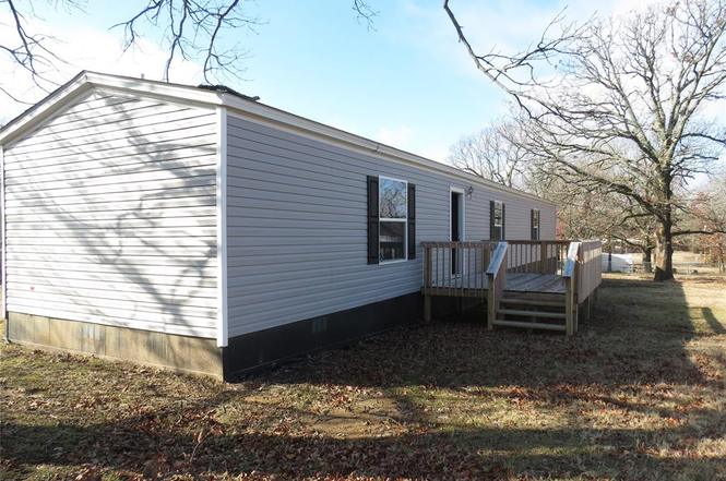 Single-story manufactured home with a raised wooden deck and leafless trees in the yard.