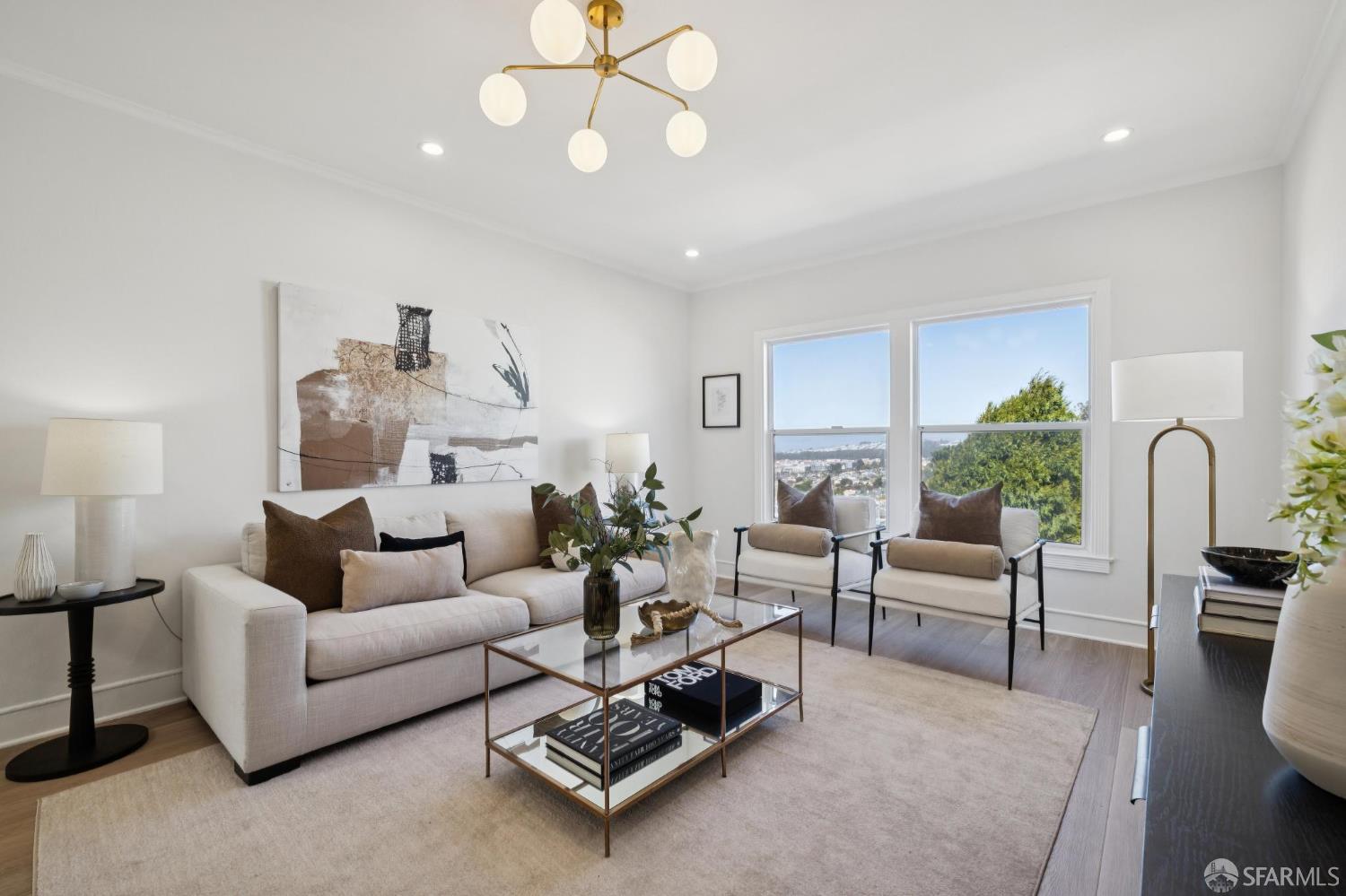 Living room with a cream sofa, two armchairs, and large windows overlooking trees and a distant city view.