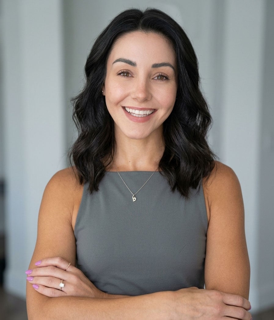 Tori Currier smiling with her arms crossed, wearing a gray sleeveless top and necklace.