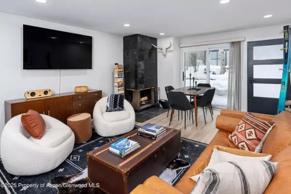 Living room with a black fireplace, rounded white chairs, and glass doors overlooking snow.
