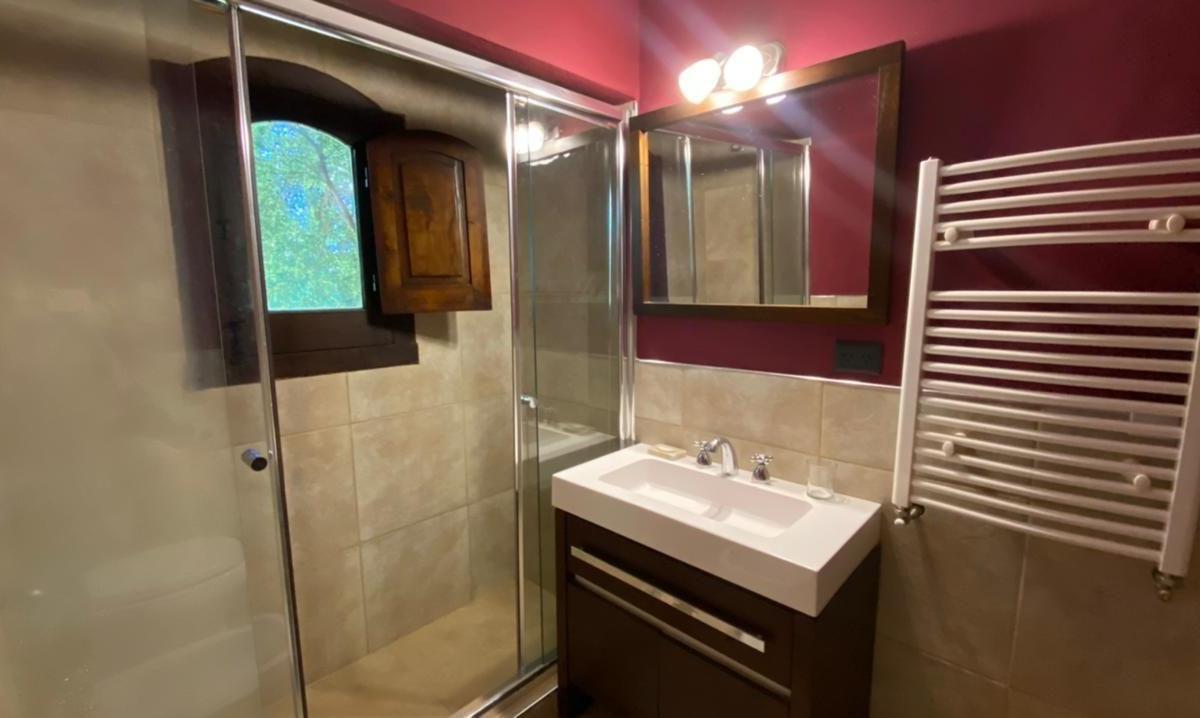 Bathroom with glass shower, dark wood vanity, burgundy walls, and an arched window with wooden shutter.