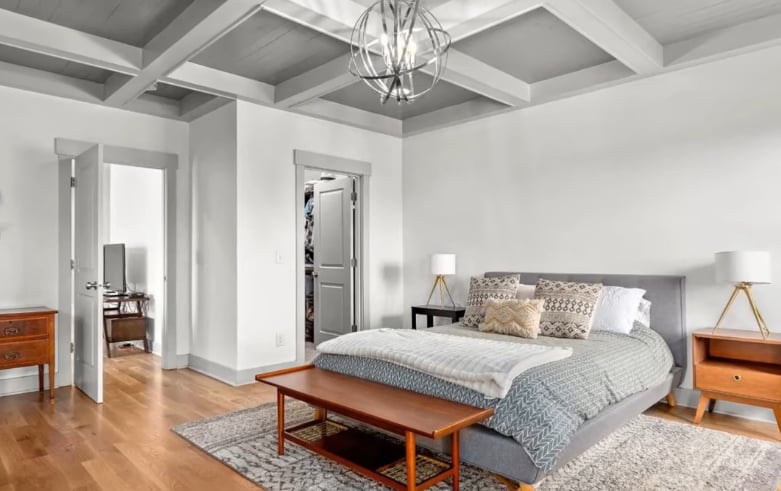 Bedroom with a gray upholstered bed beneath exposed ceiling beams and a geometric pendant light.