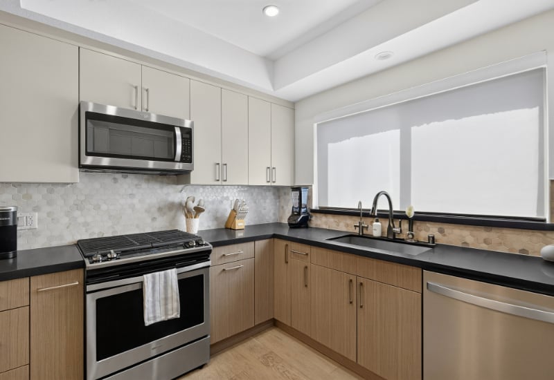 L-shaped kitchen with stainless-steel appliances, black counters, and a large shaded window.